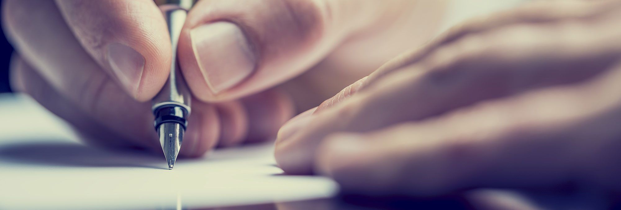 Hand mit Füllfederhalter beim Schreiben auf weißem Papier aus der Nähe fotografiert.
